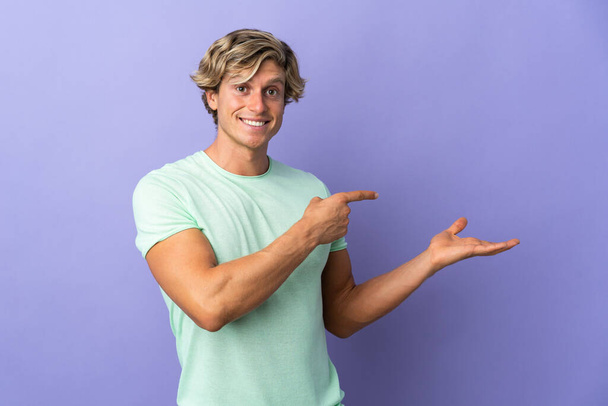 English man over isolated purple background holding copyspace imaginary on the palm to insert an ad - Photo, Image