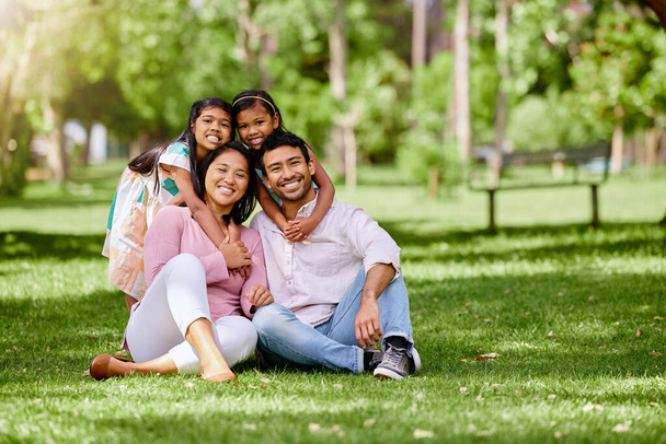 Portret szczęśliwej azjatyckiej rodziny w parku. Urocze dziewczynki łączą się i przytulają rodziców w parku. Mąż i żona siedzą i cieszą się wolnym czasem ze swoimi córkami. - Zdjęcie, obraz