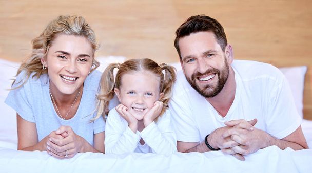 Portrait of happy carefree caucasian family lying cosy on bed while bonding together at home. Loving parents spending quality time with little daughter. Cute kid enjoying lazy morning with mom and dad - Photo, Image
