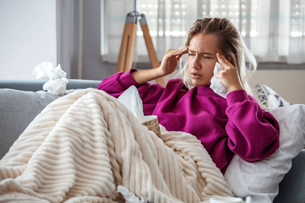 Sick woman with headache sitting under the blanket. Sick woman with seasonal infections, flu, allergy lying in bed. Sick woman covered with a blanket lying in bed with high fever and a flu, resting. - Fotoğraf, Görsel