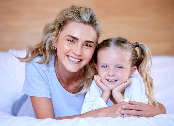 Portrait of happy caucasian mother and daughter lying on bed at home. Cheerful woman with little girl enjoying a cosy and lazy relaxing day. Loving parent bonding and sharing quality time with kid. - Photo, image