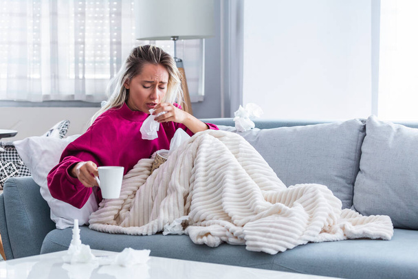 Sick Woman.Flu.Woman Caught Cold. Sneezing into Tissue. Headache. Virus .Medicines. Young Woman Infected With Cold Blowing Her Nose In Handkerchief. Sick woman with a headache sitting on a sofa - Fotoğraf, Görsel