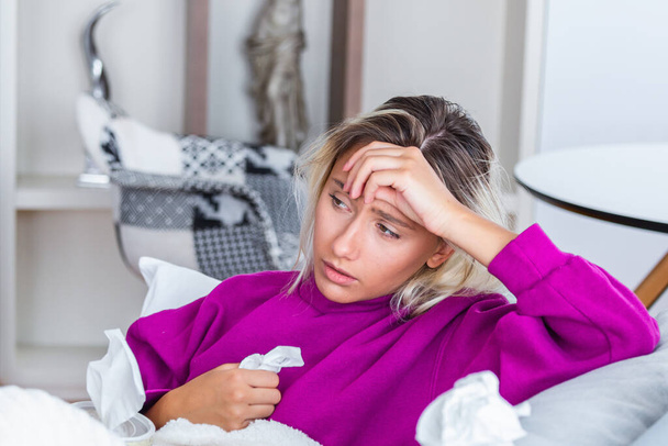 Sick woman with headache sitting under the blanket. Sick woman with seasonal infections, flu, allergy lying in bed. Sick woman covered with a blanket lying in bed with high fever and a flu, resting. - Foto, Bild