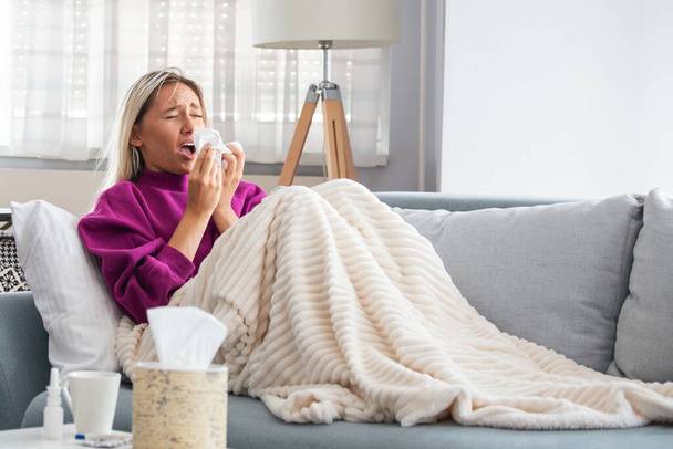 Sick Woman.Flu.Woman Caught Cold. Sneezing into Tissue. Headache. Virus .Medicines. Young Woman Infected With Cold Blowing Her Nose In Handkerchief. Sick woman with a headache sitting on a sofa - Photo, Image