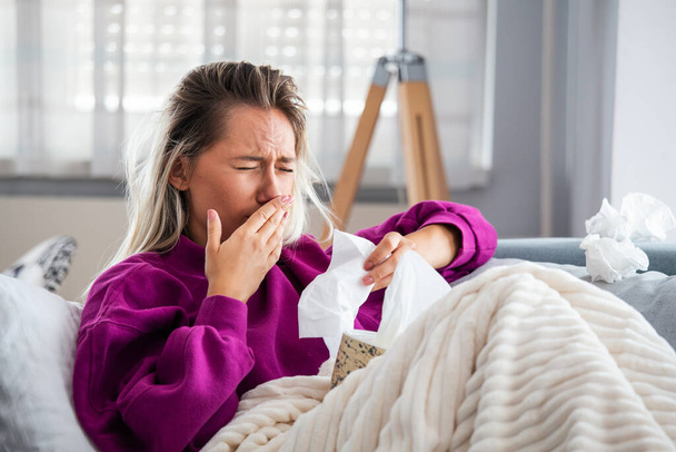 Sick desperate woman has flu. Rhinitis, cold, sickness, allergy concept. Pretty sick woman has runnning nose, rubs nose with handkerchief. Sneezing female. Brunette sneezing in a tissue - Photo, Image