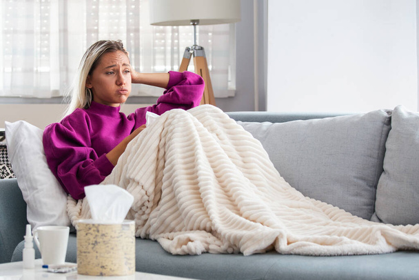 Sick Woman.Flu.Woman Caught Cold. Sneezing into Tissue. Headache. Virus .Medicines. Young Woman Infected With Cold Blowing Her Nose In Handkerchief. Sick woman with a headache sitting on a sofa - Photo, image
