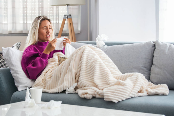 Sick woman with headache sitting under the blanket. Sick woman with seasonal infections, flu, allergy lying in bed. Sick woman covered with a blanket lying in bed with high fever and a flu, resting. - Foto, Imagem