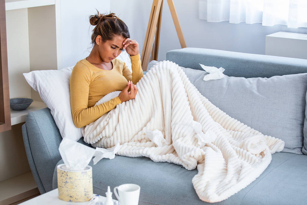 Weak woman, wearing casual clothes is sitting on a sofa and taking a pill. Sick day at home. Young woman has common cold. Sickness, seasonal virus problem concept. - Photo, Image