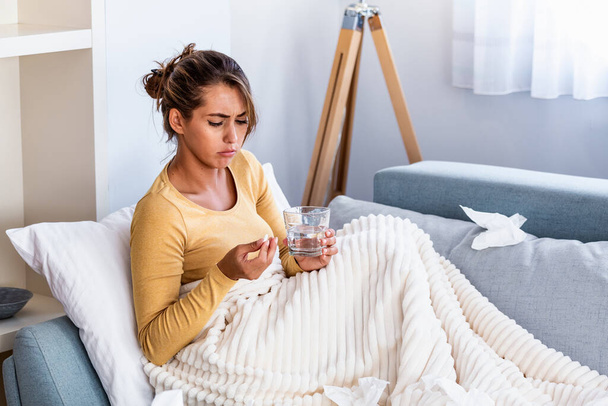 Millennial ill sick woman taking painkiller medicine to relieve stomachache pain sit on bed in the morning. Sick woman lying in bed with high fever. Cold flu and migraine. - 写真・画像