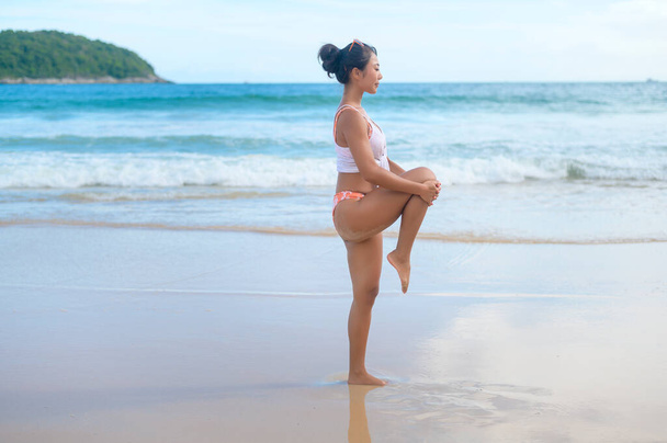 A Young asian woman in bikini doing yoga on the beach, health and meditation concept  - Photo, Image