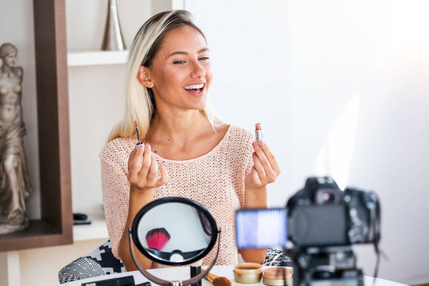 Famous blogger. Cheerful female vlogger is showing cosmetics products while recording video and giving advices for her beauty blog. Focus on digital camera - Photo, Image