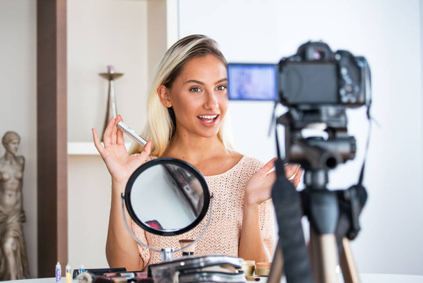 Young lady talking on cosmetics holding a makeup palette while recording her video. Woman making a video for her blog on cosmetics. - Fotó, kép
