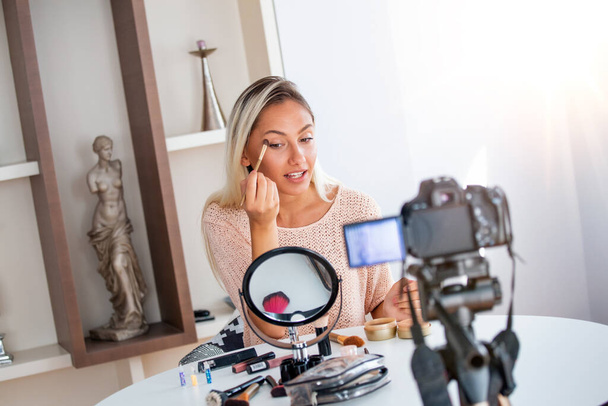 Jonge mooie blonde vrouw professionele schoonheid vlogger of blogger opname make-up tutorial om te delen op sociale media - Foto, afbeelding