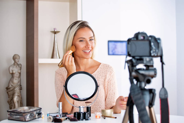 Genç güzel sarışın kadın profesyonel güzellik blogcusu veya blog yazarı sosyal medyada paylaşmak için makyaj yapıyor. - Fotoğraf, Görsel