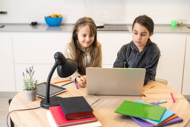 Kaksi lapsi tyttö opiskelijat opiskelevat verkossa opettajan kanssa videopuhelu yhdessä. Sisarukset ovat kotiopetuksessa tietokoneen kanssa karanteenin aikana Covid 19 pandemian vuoksi - Valokuva, kuva