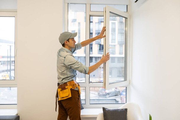 строитель устанавливает окно в доме. - Фото, изображение