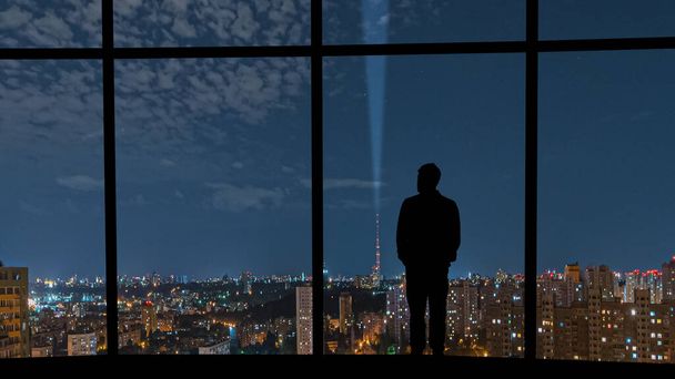 O homem que está perto da janela panorâmica contra a cidade noturna - Foto, Imagem