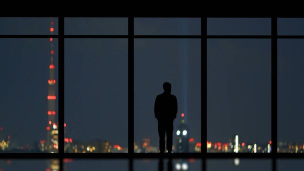 Человек, стоящий рядом с панорамным окном на фоне города - Фото, изображение