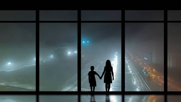 Il ragazzo e la ragazza in piedi vicino alla finestra panoramica contro la città di notte - Foto, immagini