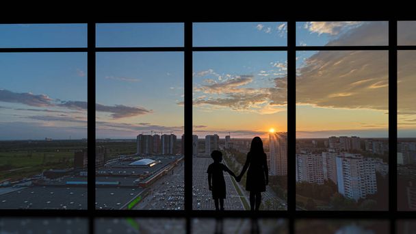 Мальчик и девочка стоят рядом с панорамным окном на фоне заката - Фото, изображение