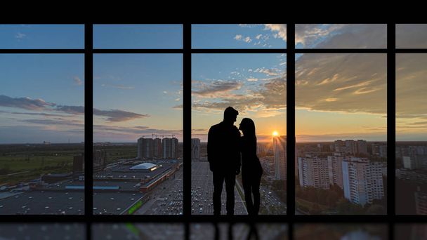 夕日の背景のパノラマの窓の近くに立っているカップル - 写真・画像