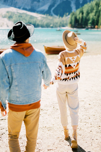 El hombre y la mujer en sombreros caminan hacia el lago Braies. Vista trasera. Foto de alta calidad - Foto, imagen