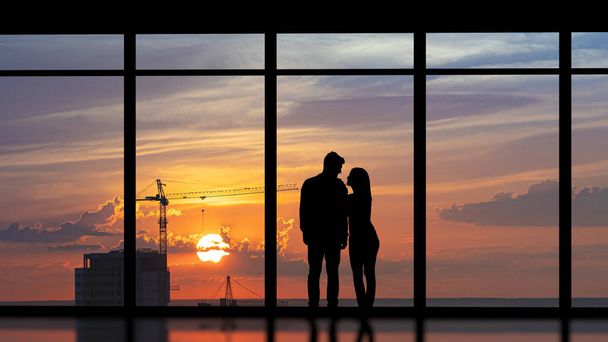 Пара, стоящая у панорамного окна на закат города - Фото, изображение