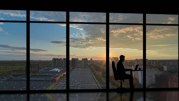 Бизнесмен сидит у панорамного окна с городским закатом - Фото, изображение