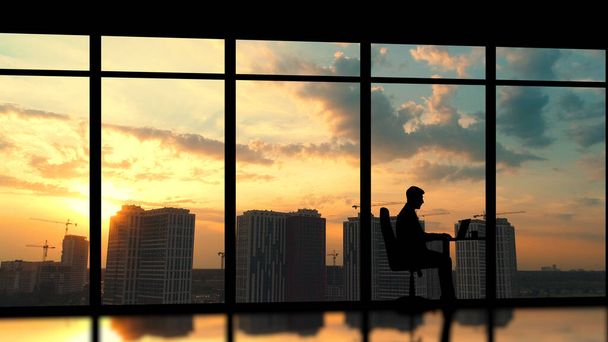 Der Geschäftsmann sitzt an einem Panoramafenster vor einem Sonnenuntergang in der Stadt - Foto, Bild