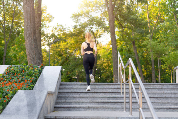 Sport and Fitness. Fit Woman Running up stairs Summer Sunny Morning Caucasian Athletic Female Jogging Outdoor Cardio Training Active Healthy Lifestyle Dressed Black Sportswear Motivation Concept - Φωτογραφία, εικόνα
