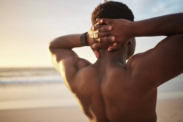 Back of a fit muscle man with hands behind his head, at the beach looking at the view during sunset. Rear view of a fitness guy thinking or bodybuilder staring at the open sky and stretching. - Fotoğraf, Görsel