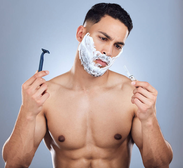Shot of a young man unable to decide between razors against a studio background. - Foto, Bild