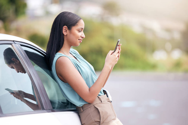 Woman leaning on a car texting. Businesswoman using a cellphone to scroll online. Businesswoman texting vehicle repair service. Businesswoman broken car. Businesswoman standing by car using smartphone - Photo, Image