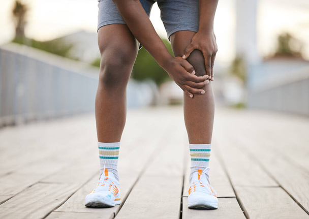 Ένας άντρας αρπάζει το γόνατό του από τον πόνο της άσκησης. Ένας Αφρο-Αμερικανός δρομέας σκύβει, αρπάζοντας το γόνατό του από τον πόνο.. - Φωτογραφία, εικόνα