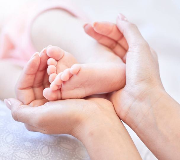 Mother holding baby feet. Closeup of tiny newborn baby feet held by a parent. Small baby toes. Little baby lying on a bed. Woman holding feet of little baby girl. Innocent infant being held by mother. - Foto, imagen