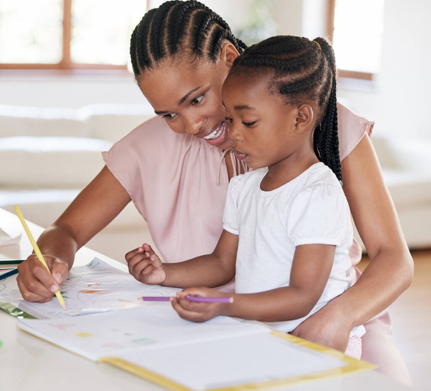 Молодая африканская американская мать помогает дочери с домашним заданием. Маленькая девочка рисует с мамой дома. Черная женщина показывает своей дочери, как писать. Маленькая девочка учится рисовать. - Фото, изображение