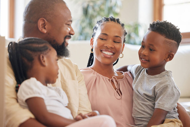 Розслаблена афро-американська сім'я посміхається, сидячи на дивані. Застрелений на молодій щасливій чорній парі, який відпочиває на дивані, розмовляючи зі своїми двома гарними дітьми вдома.. - Фото, зображення