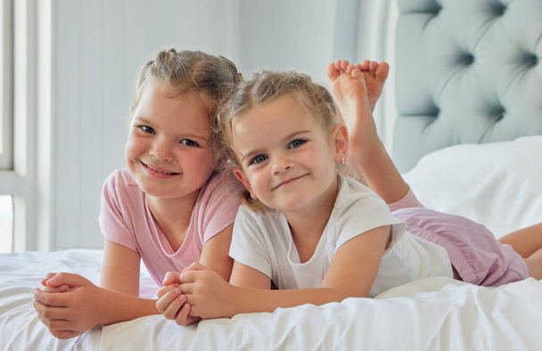 Portrait of siblings playing together. Two caucasian girls relaxing together. Sisters spend time together in their bedroom. Little girls together at home. Caucasian children lying on the bed. - Foto, imagen