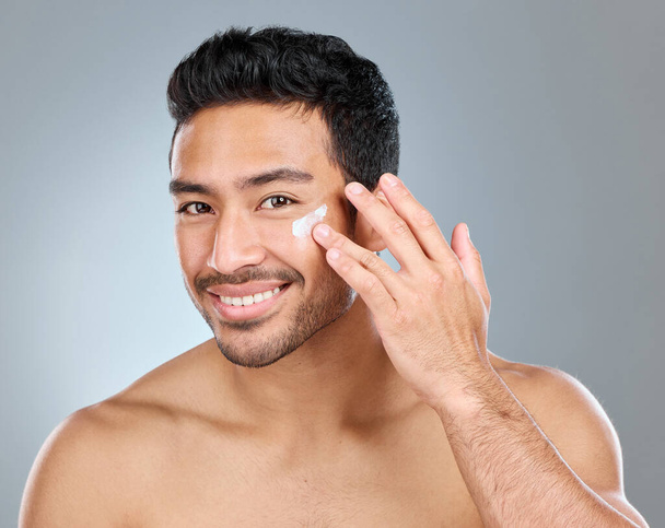 Shot of a man applying moisturiser to his face while standing against a grey background. - 写真・画像