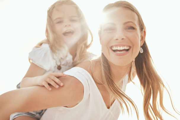 Happy caucasian mother and playful daughter having fun together in the sun. Carefree woman carrying excited girl for a piggyback ride while bonding outside. Single mom enjoying quality time with kid. - Valokuva, kuva