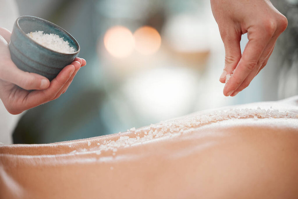 Shot of a masseuse pouring exfoliating salt scrub onto a clients back. - Foto, afbeelding