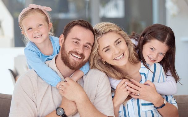 Happy caucasian family of four smiling while relaxing on a sofa together at home. Carefree loving parents bonding with two cute little daughters. Adorable young playful girls hugging mom and dad. - 写真・画像