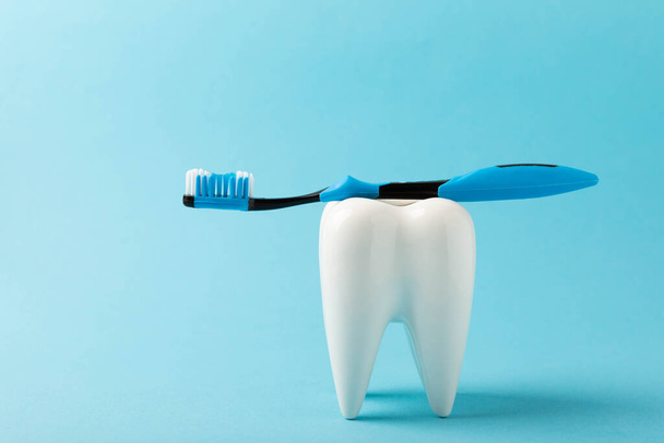 Cleaning model of a white tooth with a toothbrush on a blue background. The concept of dental hygiene. Prevention of plaque and gum disease.MOCKUP - Photo, Image