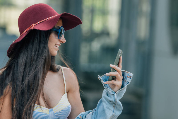 αστικό στυλ hipster κορίτσι το καλοκαίρι κοιτάζοντας το κινητό τηλέφωνο στο δρόμο - Φωτογραφία, εικόνα