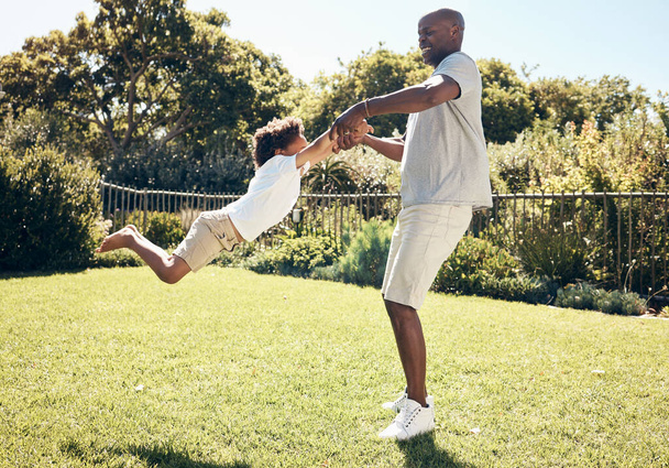Neşeli Afro-Amerikan babası oğlunu kollarından tutuyor. Baba oğluyla parkta ya da güneşli bir günde arka bahçelerinde oynarken oynuyor.. - Fotoğraf, Görsel