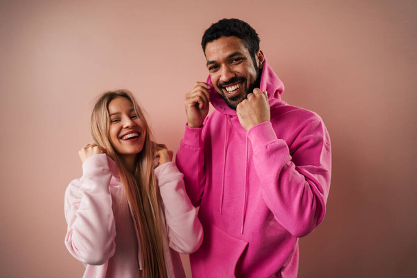 A fashion studio portrait of a happy young blonde woman in hoodie posing over pink background. - Fotó, kép