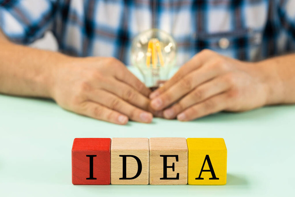 Colorful wooden blocks with the words Idea, Man holding a light bulb in his hand, Creative concept - Foto, imagen
