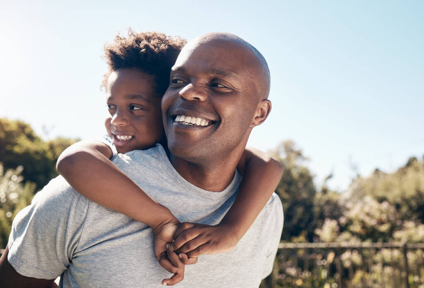 Mutlu bir Afrikalı Amerikalının genç oğluyla yakınlaşması yakındır. İki siyah erkek baba ve oğul mutlu ve pozitif görünürken sevgi dolu davranıyorlar ve parkta yürüyorlar.. - Fotoğraf, Görsel