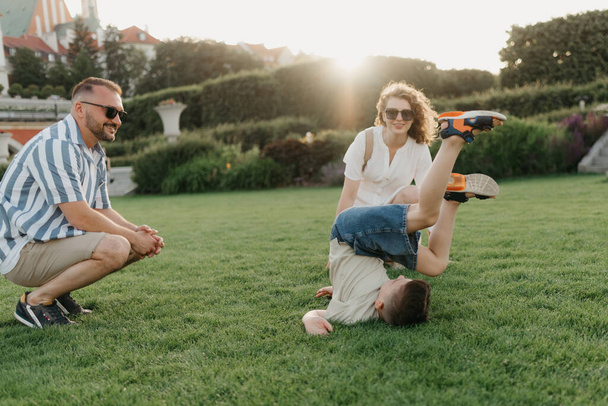 Father, mother, and son are having fun in the garden of an old European town. Happy family in the evening. A boy is showing somersaults to his parents in the background of the palace at sunset. - Foto, immagini
