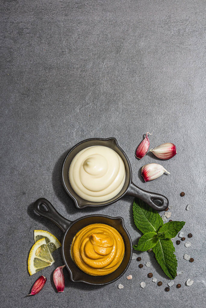 Mustard and mayonnaise sauces. Fresh mint, lemon, garlic, and spices. A hard light, dark shadow, stone concrete background, flat lay, top view - Photo, Image